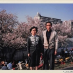 1986-04-13 東京都大田区六郷土手 多摩川の土手で桜を背景に立っているおじいちゃんとおばあちゃん